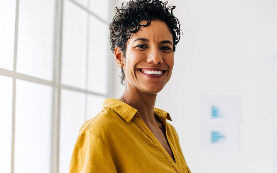 A middle aged woman smiles in a room with a blurred background.