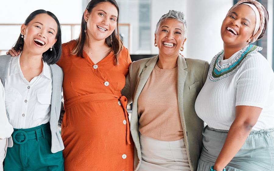 Four women of diverse backgrounds and ages smile together. 