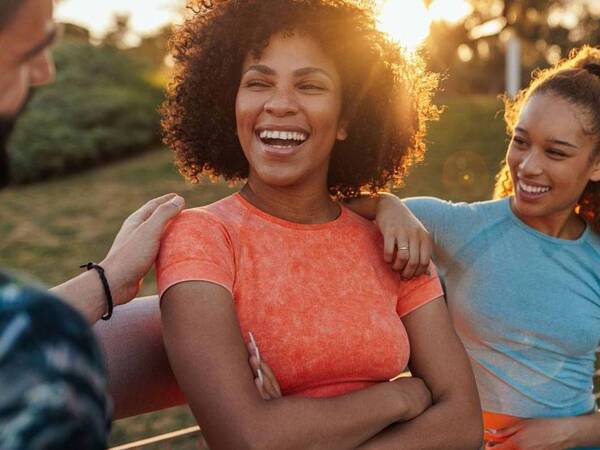 A group of young men and women wearing fitness outfits smile as they gather to do an outdoor workout.