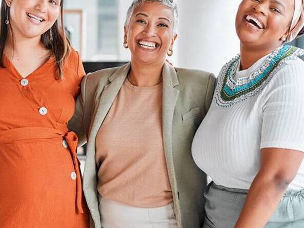 Four women of diverse backgrounds and ages smile together. 